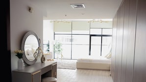 A modern bedroom with a vanity, a large mirror, a bed, and a view of the outdoors. - Bright Studio with Rooftop Pool & Gym (Dubai)