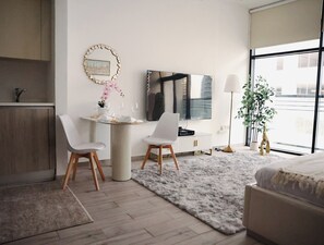 A modern hotel room with a dining area, a large window, and a bed. - Bright Studio with Rooftop Pool & Gym (Dubai)