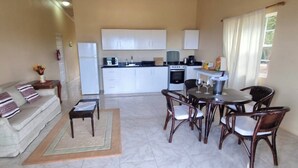 A compact living space with a sofa, dining table, chairs, a kitchen area with cabinets and appliances, and a window with curtains. - Castles in Paradise #C5 - by ZenBreak (Savannes)