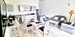A compact living space with a kitchenette, a dining area with a table and chairs, a sofa, and a lamp.