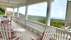 A covered outdoor seating area with white chairs and a small table, overlooking a scenic landscape.