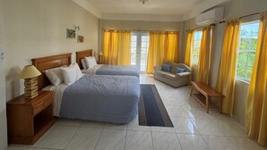A hotel room with two beds, a sofa, a bench, and a view of greenery outside.