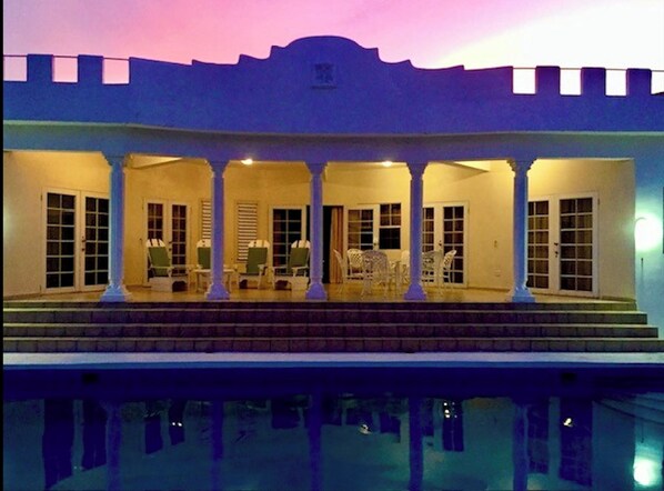 Un edificio con un patio cubierto, columnas y una piscina.