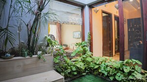 Een kleine binnenplaats met plantenpotten, een gestreept bankje en een glazen deur naar een kamer.