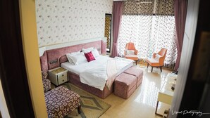 Een slaapkamer met een bed, nachtkastje, stoel en poef.