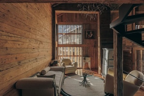 Ein Innenraum einer Blockhütte mit einer Couch, Sesseln, einem Kamin und einem großen Fenster.