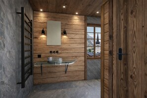 Un baño con pared de madera, lavamanos de vidrio y ventana con vista a un edificio.