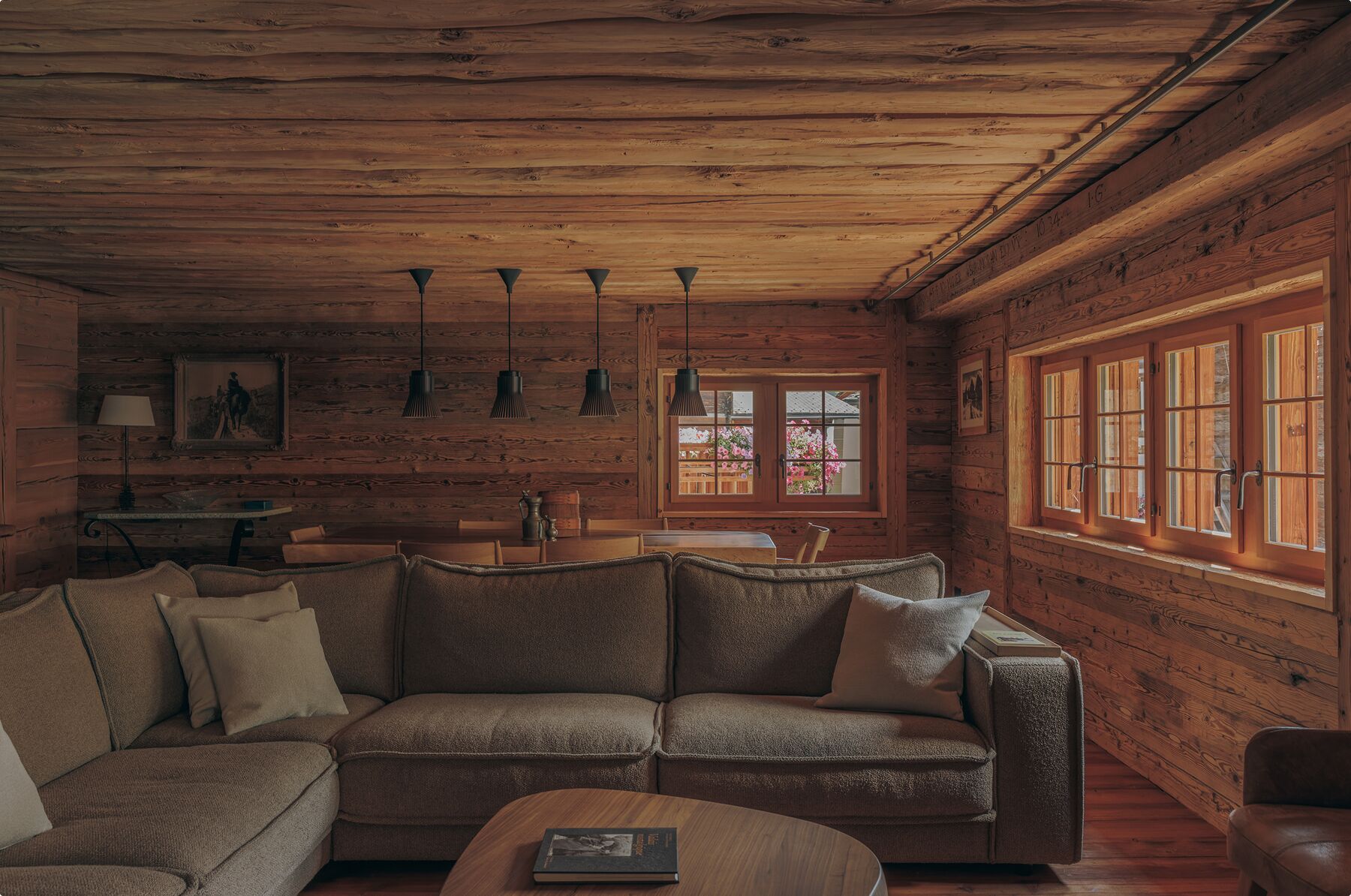 Ein gemütliches Blockhaus-Interieur mit Holzbalkendecke, einer Couch, einem Couchtisch und einem Fenster mit Aussicht.