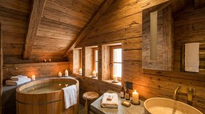 Interior de una cabaña de madera con bañera de madera, lavabo y ventana con velas.