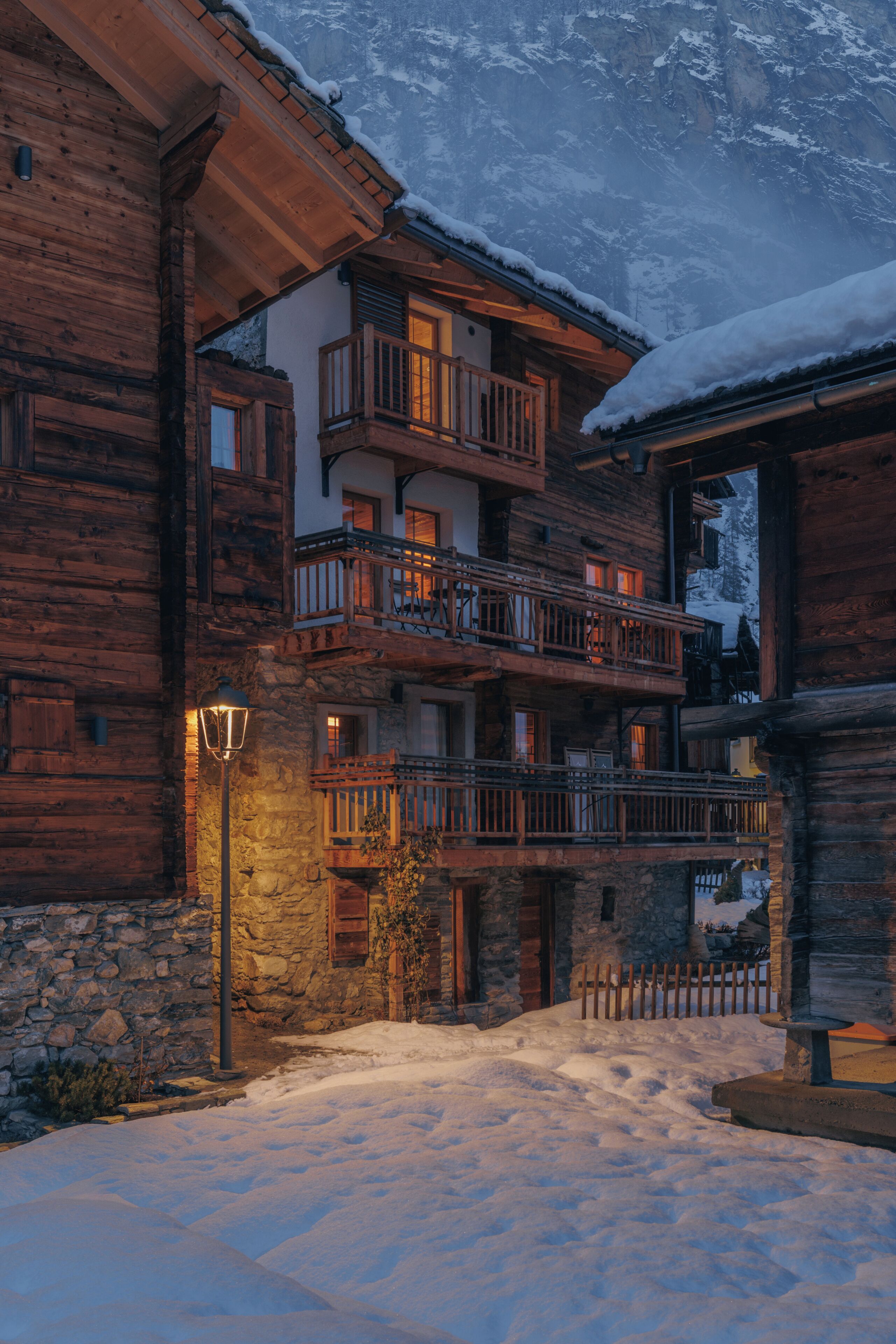 Eine Holzhütte mit mehreren Balkonen, Steinwänden und verschneitem Gelände.