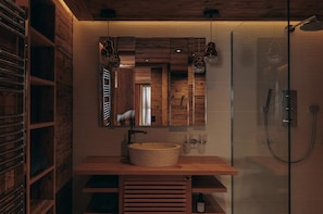 Ein modernes Badezimmer mit einem Holzbettchen, einem großen Spiegel und einer Duschkabine.