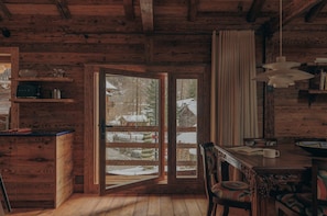 Ein Holzblockhaus-Interieur mit Essbereich, einer Küche inklusive eingebauter Mikrowelle und einer großen Glasschiebetür, die zu einer verschneiten Außenanlage führt.