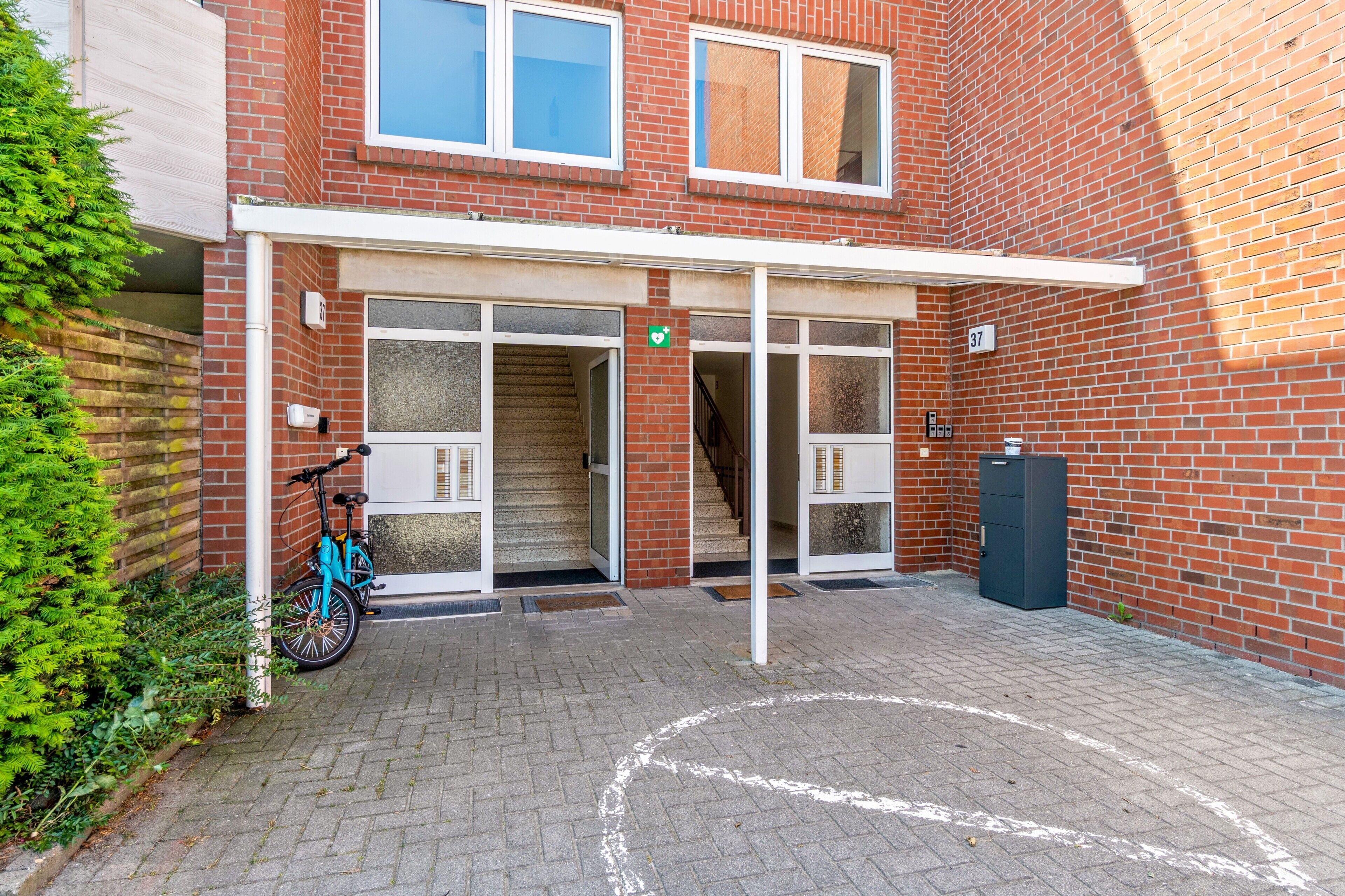 Ein Gebäudeeingang mit überdachter Veranda, einer Treppe und einem draußen abgestellten Fahrrad.