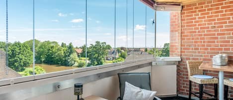 Ein Balkon mit Blick auf einen Fluss, ein Tisch mit Stühlen und ein hängender Vogel.