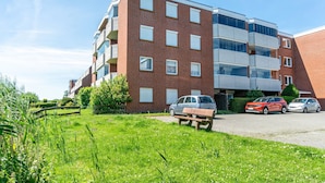 Un edificio in mattoni di più piani con balconi, un'area di parcheggio e un prato antistante.