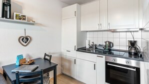 Una cucina compatta con mobili bianchi, un piano di lavoro nero e un forno in acciaio inossidabile.