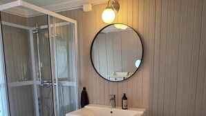 A bathroom with a glass shower enclosure, a white sink with a round mirror, and a toilet. - Spacious house in peaceful countryside - perfect for hiking, fishing and relaxation (Møre og Romsdal)