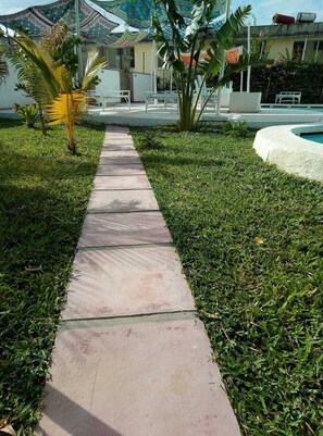 A pathway leading to a building with a pool, surrounded by grass and palm trees. - Stylish Home Away from Home (Diani Beach)