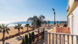 Un balcon avec vue sur une plage, des palmiers et un ciel dégagé.