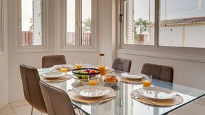 Une table à manger avec des chaises, des assiettes, des verres et un saladier de fruits.