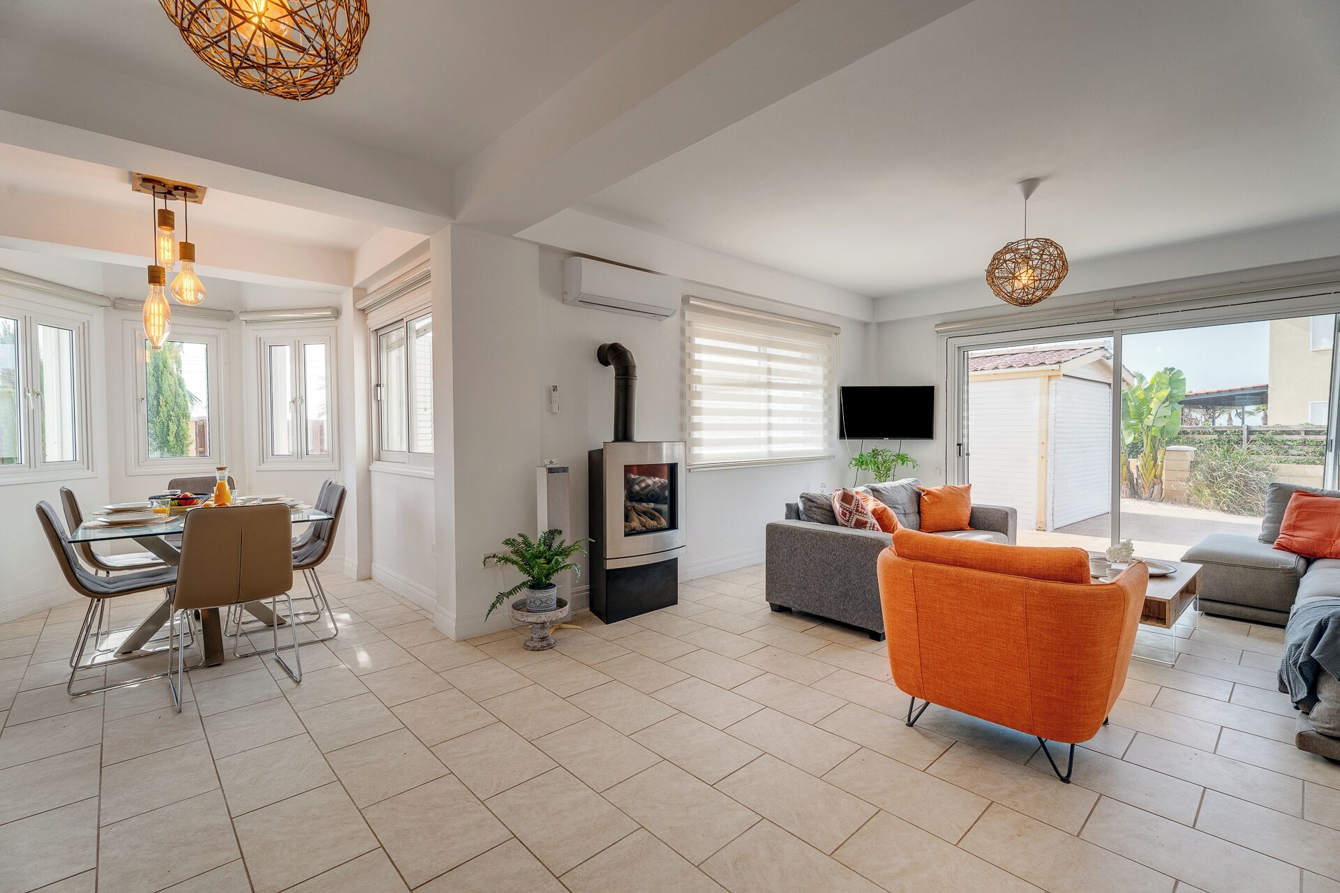 Una sala de estar moderna con chimenea, un comedor y un sofá con cojines naranjas.