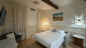 Een hotelkamer met een bed, een stoel, een nachtkastje, een spiegel en een schilderij aan de muur.