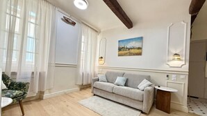 Een woonkamer met een bank, een klein rond tafeltje, een houten vloer en een schilderij aan de muur.