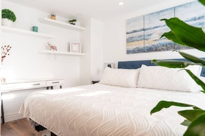 Ein Schlafzimmer mit einem Bett, einem Schreibtisch, Regalen mit Pflanzen und einem Bild an der Wand.