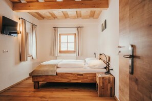 Une chambre à coucher avec un lit en bois, une fenêtre avec des rideaux, un téléviseur fixé au mur et une porte avec une poignée.