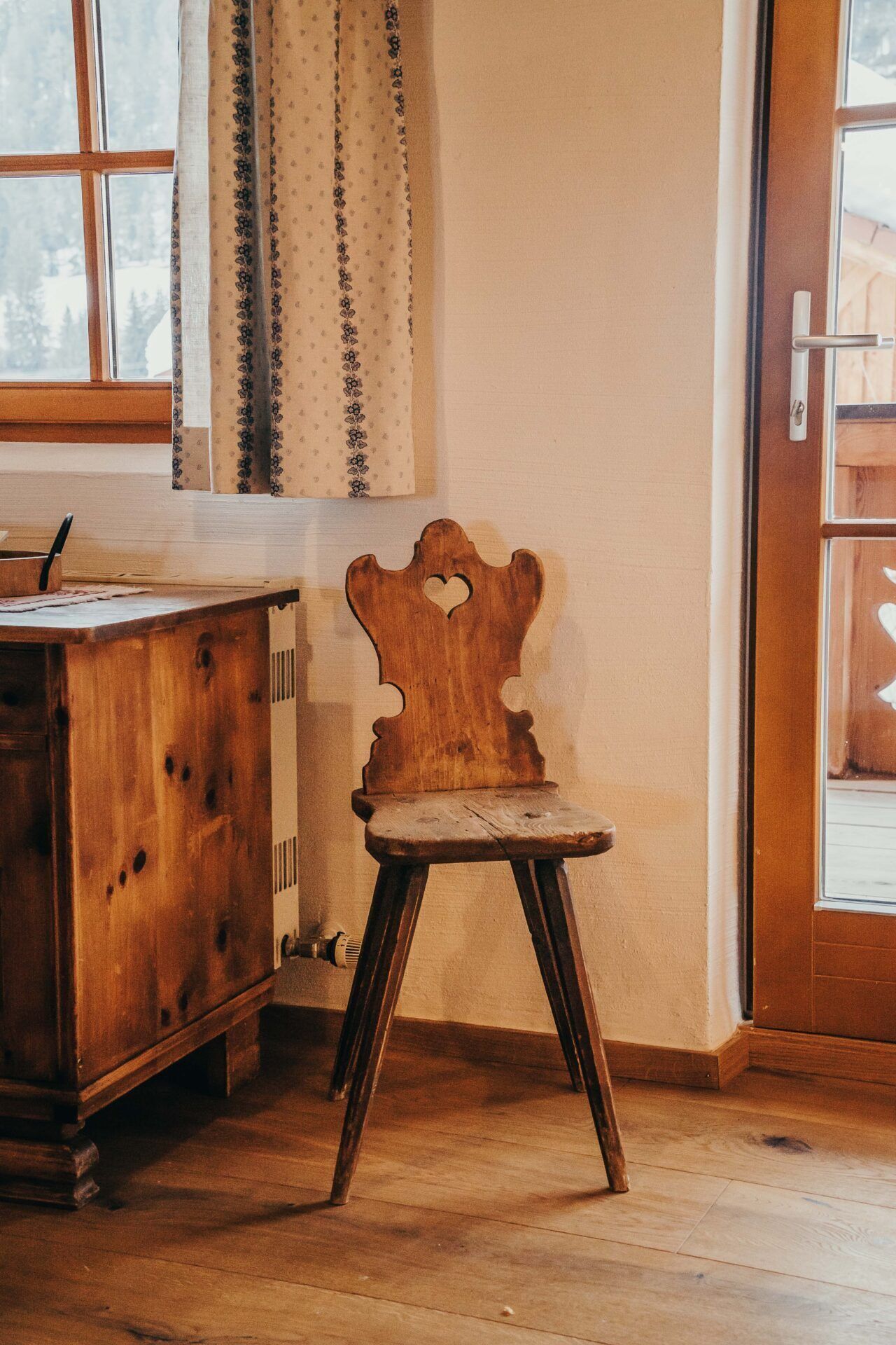 A wooden chair with a heart-shaped cutout in the backrest, positioned next to a wooden desk with a pen holder.