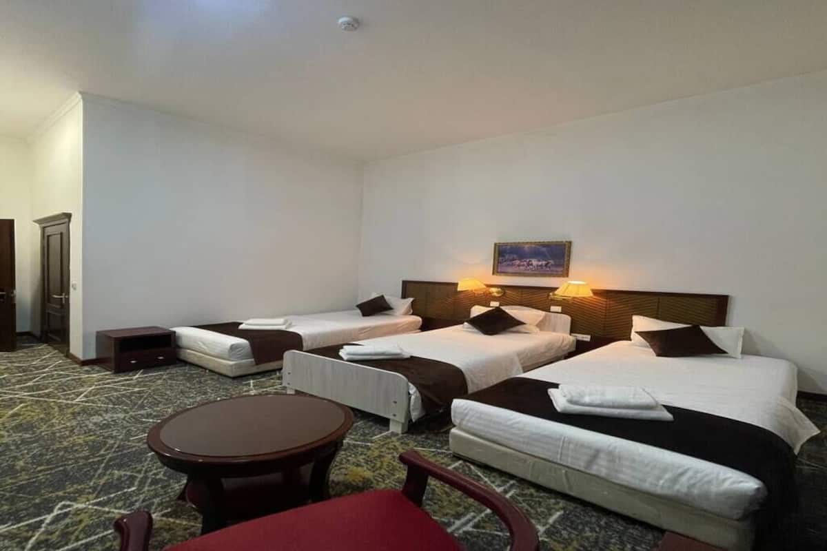 A hotel room with two single beds, a small table, a chair, and a headboard with a picture.