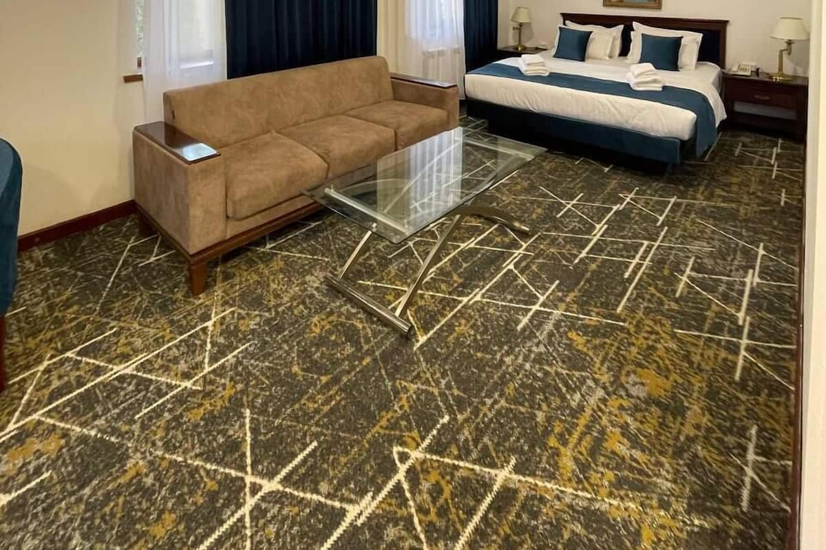 A hotel room with a sofa, a bed with a blue and white bedspread, a painting on the wall, and a patterned floor.