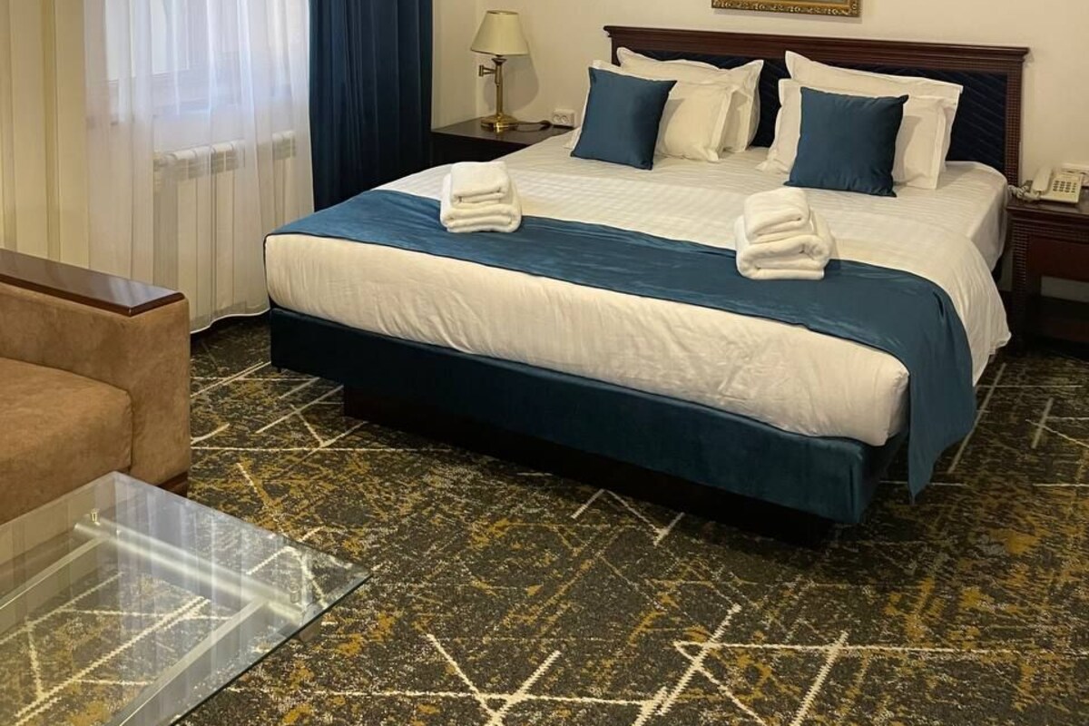 Una habitación de hotel con una cama, una mesita de noche, una lámpara, un cuadro y una alfombra estampada.