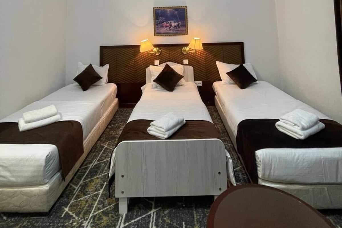 A hotel room with two single beds, a headboard with a picture, and a small table.