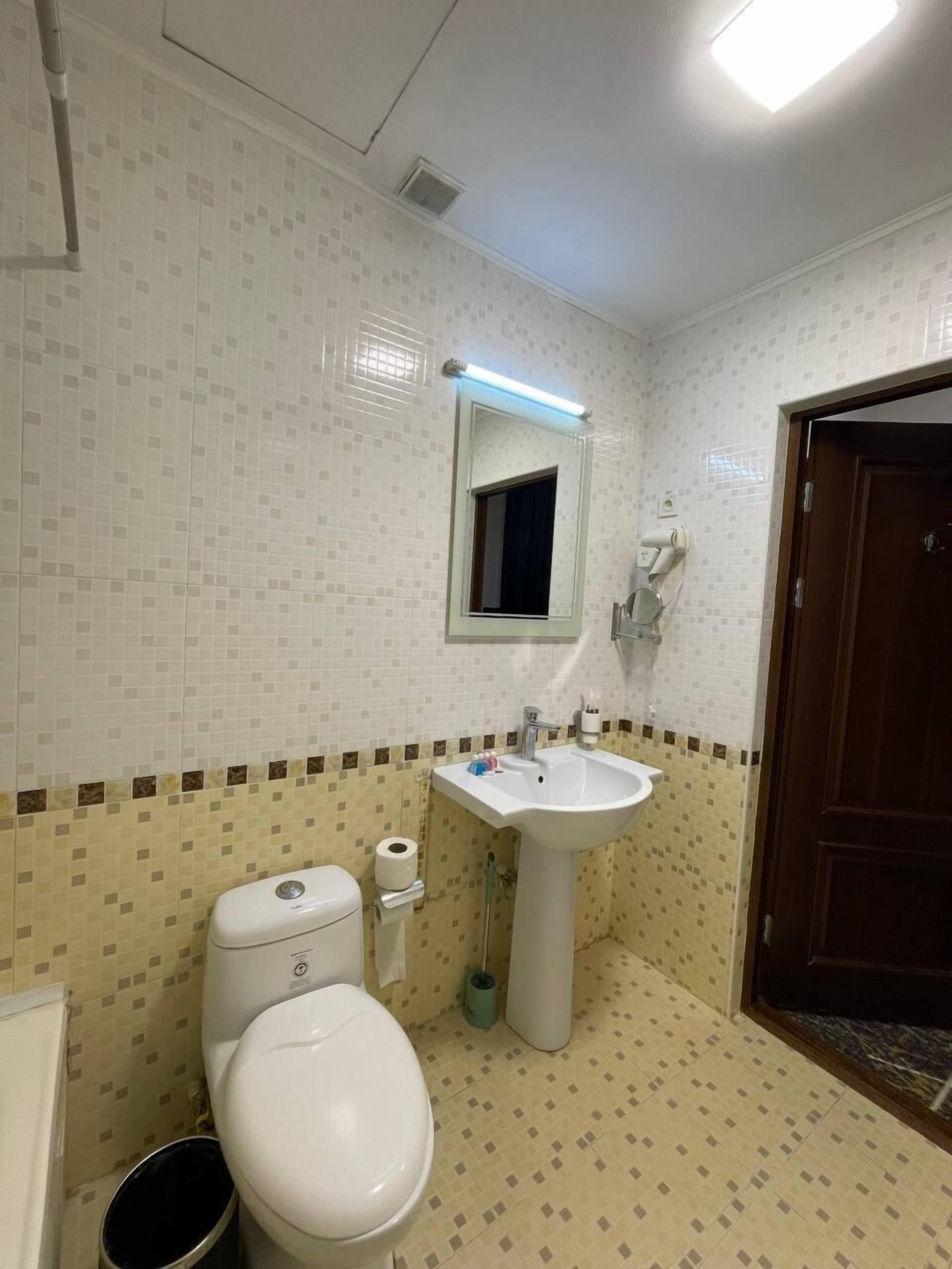 Un baño con inodoro, lavabo, espejo y baldosas de suelo estampadas.