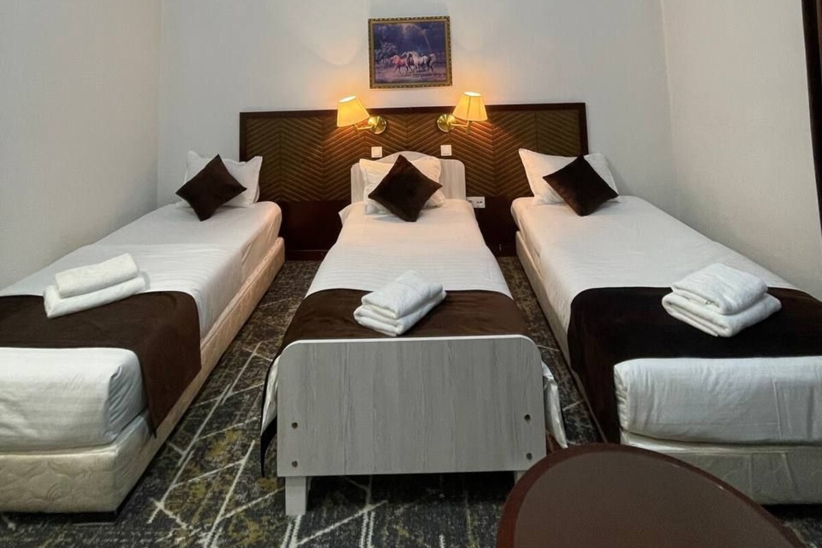 A hotel room with two single beds, a headboard with a picture, and a small table.