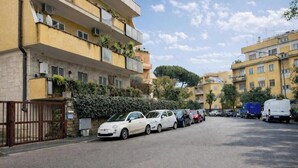 Eine Wohnstraße mit parkenden Autos, einem verschlossenen Eingang und mehrstöckigen Gebäuden mit Balkonen.