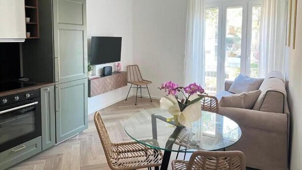 Ein Wohnzimmer mit einer Couch, einem Glastisch, einem Fernseher und einer Küchenzeile mit Schränken und einem Backofen.
