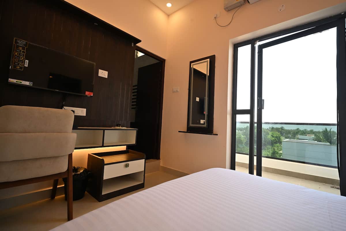 Un dormitorio con cama, escritorio, silla, espejo y vistas al exterior.