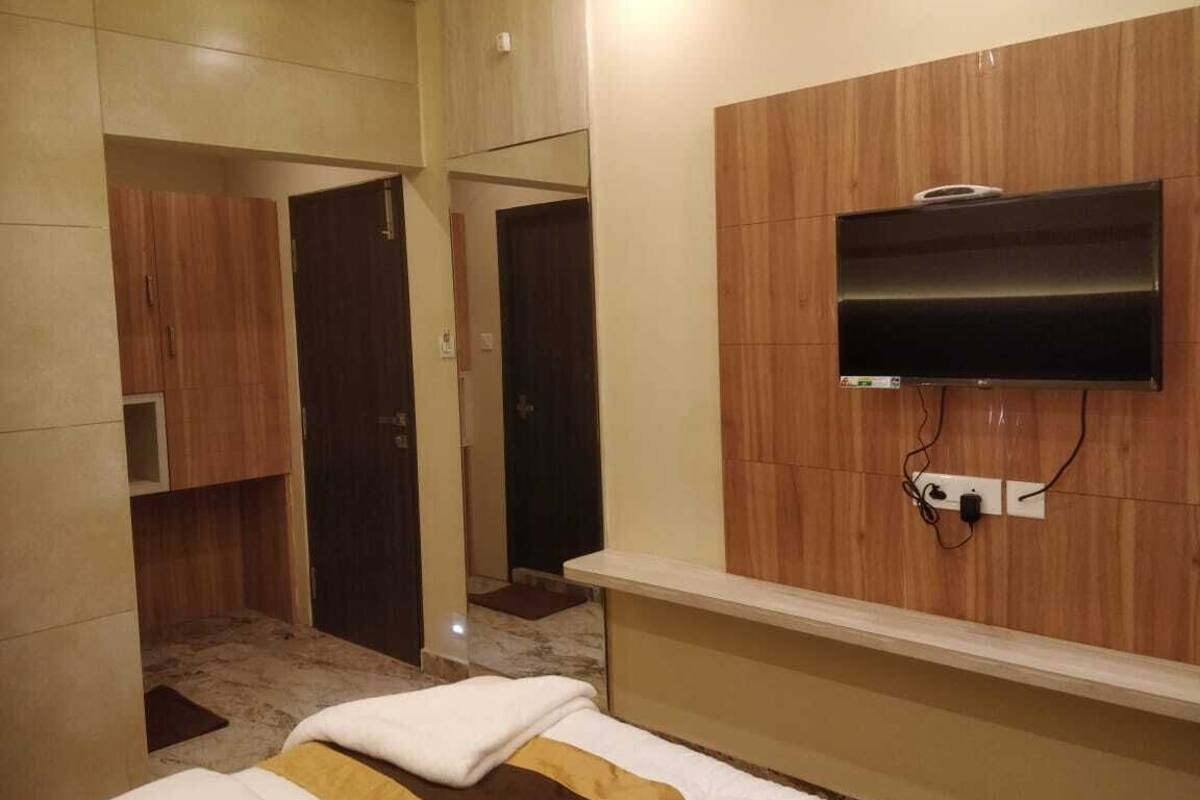 Habitación de hotel con una cama, un televisor montado en la pared y un armario de madera.
