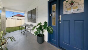A residential entrance with a blue door, a potted plant, and a patio area with a table and chairs. - Vino Cottage (Cessnock)