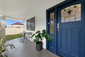 A residential entrance with a blue door, a potted plant, and a patio area with a table and chairs. - Vino Cottage (Cessnock)