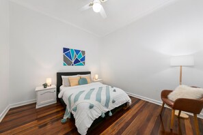 A bedroom with a bed, a nightstand, a chair, a floor lamp, and a ceiling fan. - Vino Cottage (Cessnock)