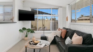 A modern living room with a black leather sofa, a round coffee table, and a flat-screen TV mounted on the wall. - Vino Cottage (Cessnock)