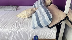 A small, single-bed room with purple walls, a white mattress, striped pillows, and a small table with a bottle and a roll of toilet paper. - Privet bedroom in share home (London)