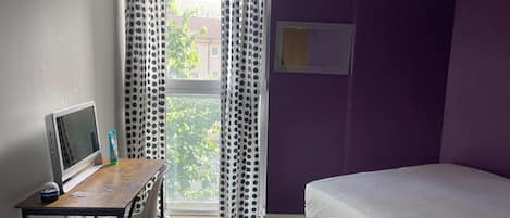 A room with a bed, a desk with a computer, and a window with curtains.