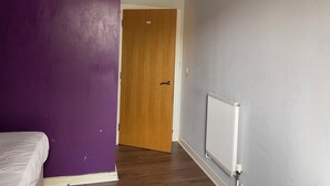A room with a purple wall, a wooden door, a radiator, and a white bed. - Privet bedroom in share home (London)