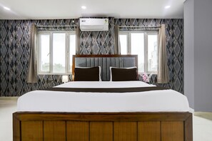 Ein Schlafzimmer mit einem großen Bett, einer Klimaanlage, gemustertem Wandpapier und Fenstern mit Vorhängen.