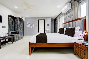 A modern hotel room with a large bed, a wooden nightstand, a desk with a chair, a ceiling fan, and an air conditioning unit. - Deluxe With Twin Bedhotel SPG Grand (Hyderabad)