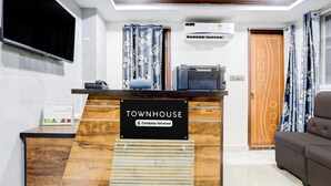 Eine Rezeption mit einem Schild, das 'TOWNHOUSE Company-Serviced' zeigt, ein wandmontierter Flachbildfernseher, eine Klimaanlage und eine Holztür mit dekorativer Gestaltung.